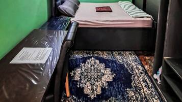 A small room with two beds, a green wall, a ceiling light, and a window.