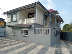 A two-story house with a balcony, a gated entrance, and a tiled driveway.