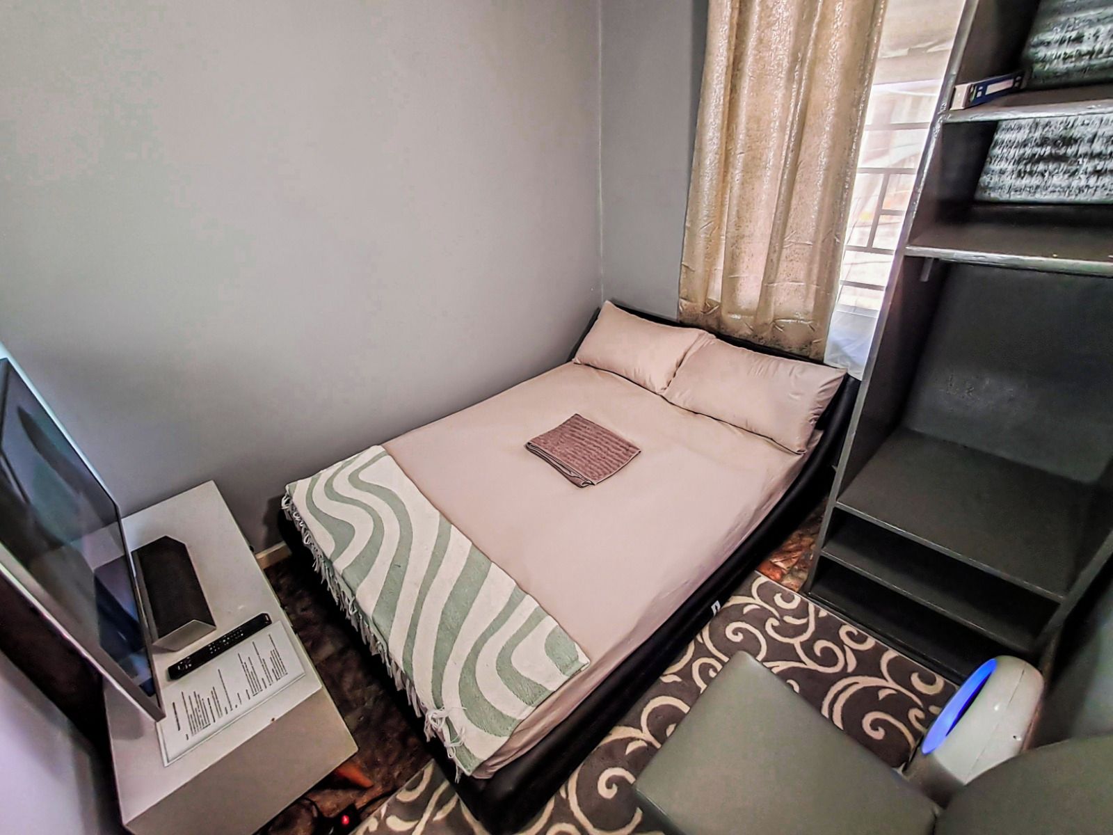 Camera d'albergo compatta con un letto, una scrivania con un computer e una sedia.