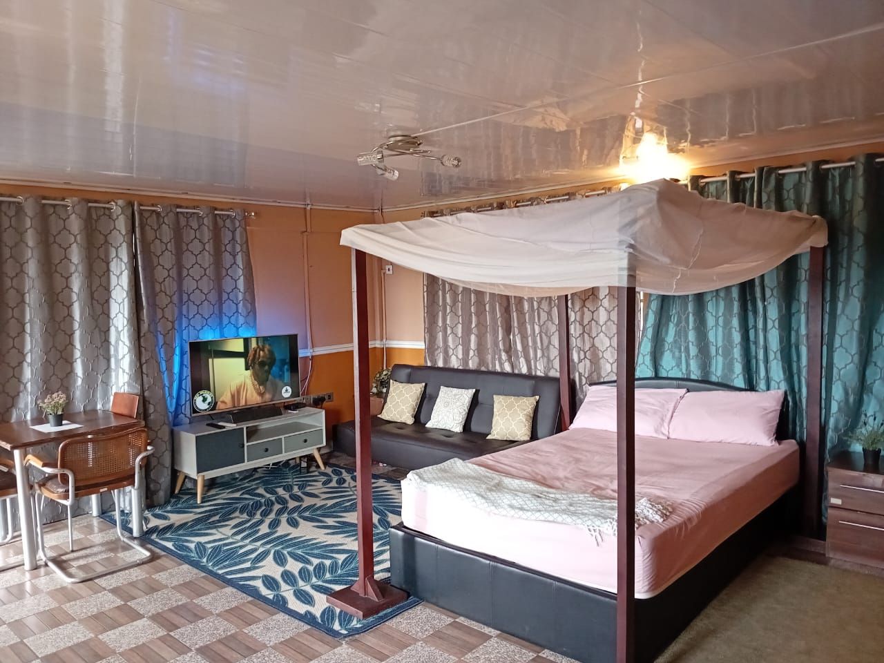 Un lit à baldaquin, un téléviseur posé sur un meuble, un bureau avec une chaise et un tapis à motifs.