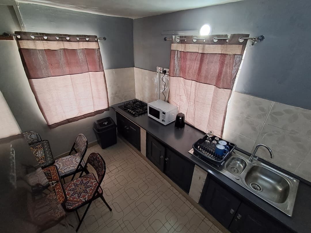 A compact kitchen with a gas stove, microwave, sink, and a dining area with patterned chairs.