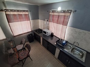Una cucina compatta con piano cottura a gas, forno a microonde, lavello e zona pranzo con sedie a fantasia.