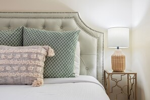 Un lit doté d’une tête de lit capitonnée, de plusieurs oreillers, d’une table de chevet en osier et d’une lampe fixée au mur.