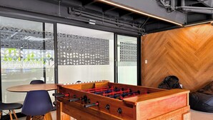 Een moderne kamer met een tafelvoetbaltafel, een wand met houten visgraatmotief en een glazen scheidingswand met een geometrisch patroon.