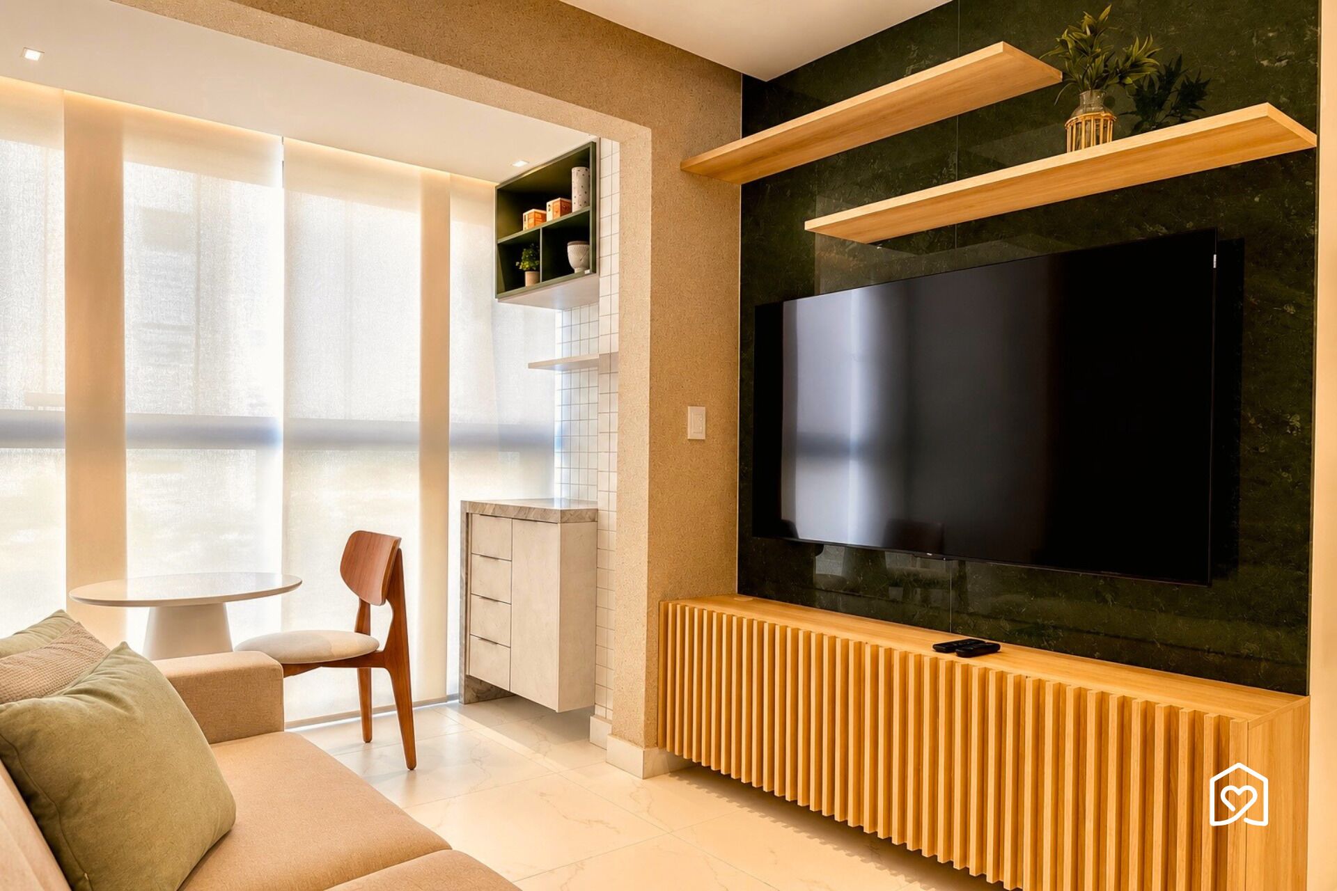 A modern living room with a large flat-screen TV, wooden shelving, a sofa, and a dining area with a kitchen in the background.