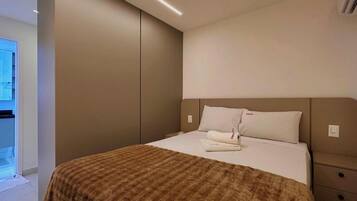 A modern hotel room with a large bed, a brown textured blanket, and a view of the outdoors.