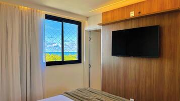 Habitació d'hotel amb llit, televisió penjada a la paret, finestra amb vista al mar i porta.