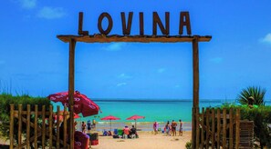 A beach entrance with the word 'LOVINA' above, wooden fencing, and red umbrellas. - NOA Residence Club - LikeHome  (Cabedelo)