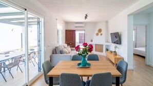 A modern living room with a wooden dining table, grey upholstered chairs, a sofa, and a TV mounted on the wall. - Cubo's Miralmonte Rural House / Private pool / Air conditioning / BBQ (Coín)