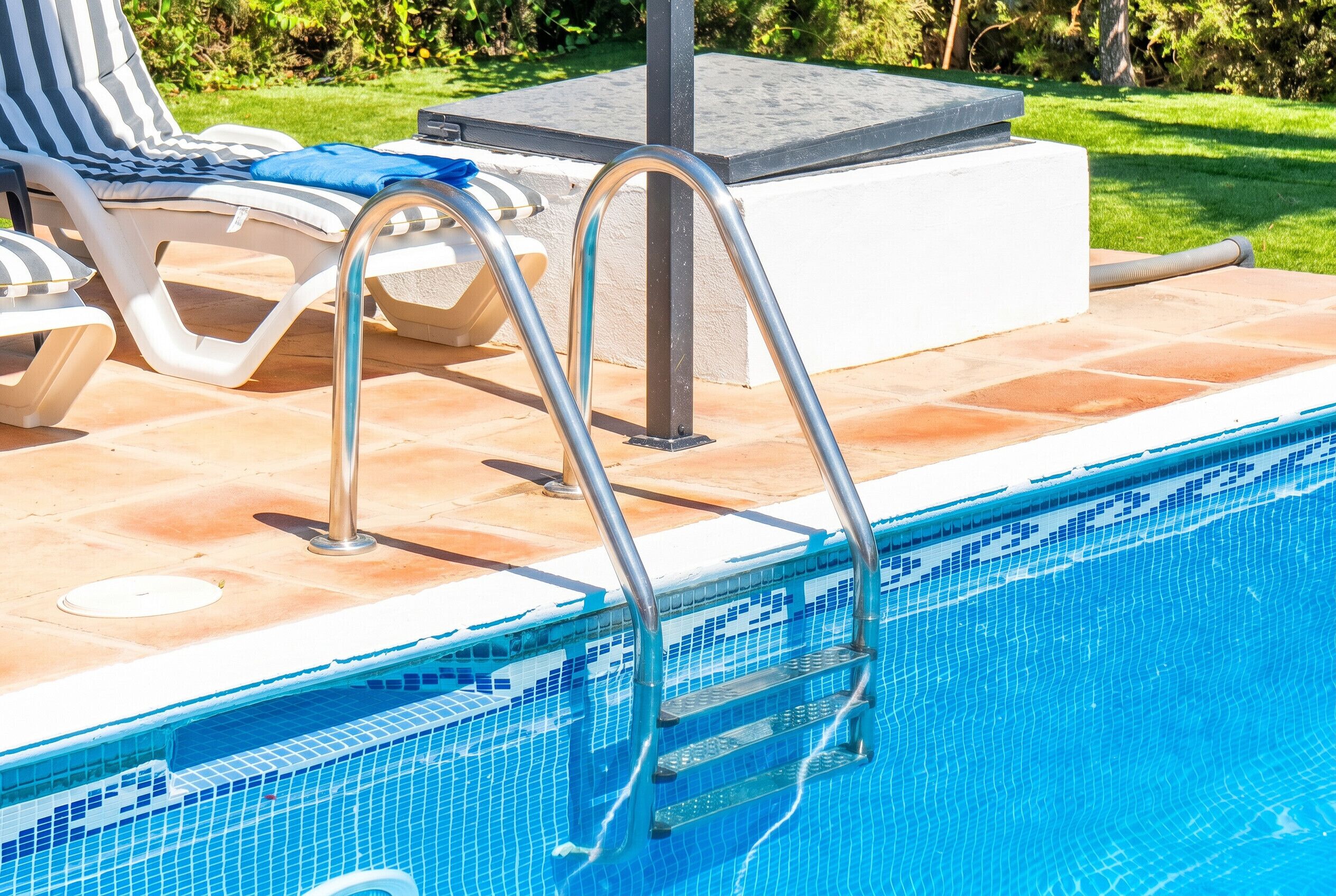 A swimming pool with a metal ladder, lounge chairs, and a tiled deck.