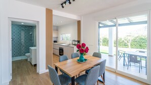 A modern kitchen with a central island, a dining area with a wooden table and chairs, and a view of a garden through large sliding doors. - Cubo's Miralmonte Rural House / Private pool / Air conditioning / BBQ (Coín)