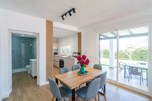 A modern kitchen with a central island, a dining area with a wooden table and chairs, and a view of a garden through large sliding doors. - Cubo's Miralmonte Rural House / Private pool / Air conditioning / BBQ (Coín)