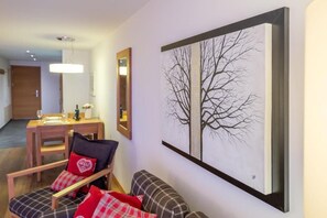 Ein Wohnzimmer mit einer Couch, einem Sessel, einem Esstisch mit Stühlen und einem großen Bild in einem Rahmen an der Wand.