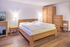 Ein hölzernes Bett mit weißer Bettwäsche in einem Zimmer mit Holzboden, einem Fernsehgerät auf einem Holzgestell und einem Holzschrank.