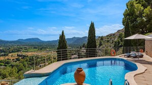A swimming pool with a view of a mountainous landscape, surrounded by a deck with lounge chairs and a potted plant. - 5-bed Villa, Two Pools, Puerto Pollenca (Pollença)