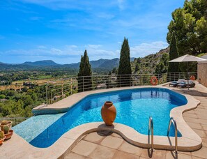 Ein Pool mit Blick auf eine gebirgige Landschaft, umgeben von einer Sonnenterrasse mit Liegestühlen und einem Blumentopf.