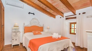 Ein Schlafzimmer mit einem Bett, Nachttischlampen, einem Beistelltisch, einem Fenster mit Vorhängen und einer Holzbalkendecke.