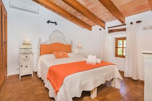 Ein Schlafzimmer mit einem Bett, Nachttischlampen, einem Beistelltisch, einem Fenster mit Vorhängen und einer Holzbalkendecke.