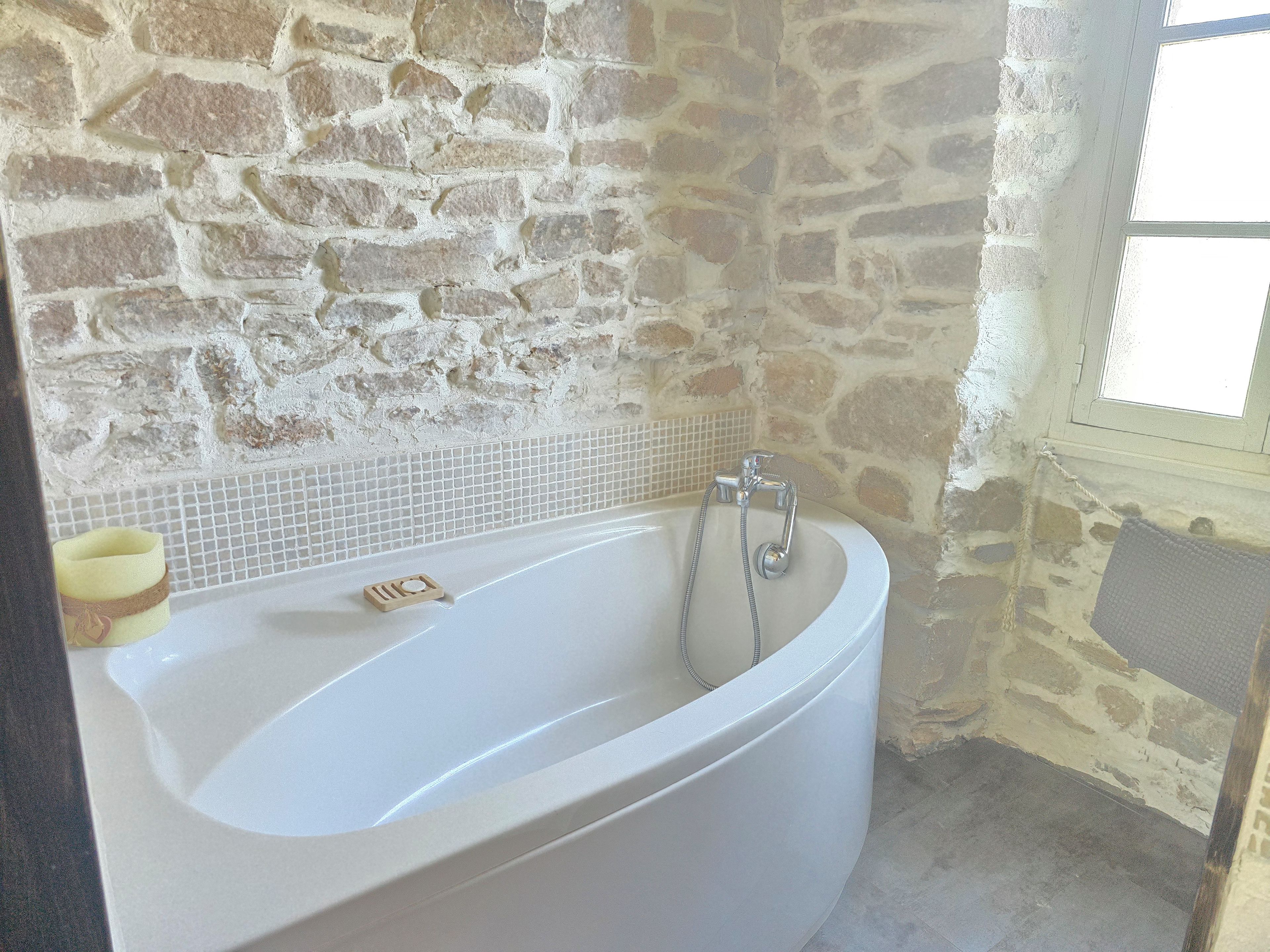 Ein Badezimmer mit Steinwand, einer Badewanne und einem Fenster.