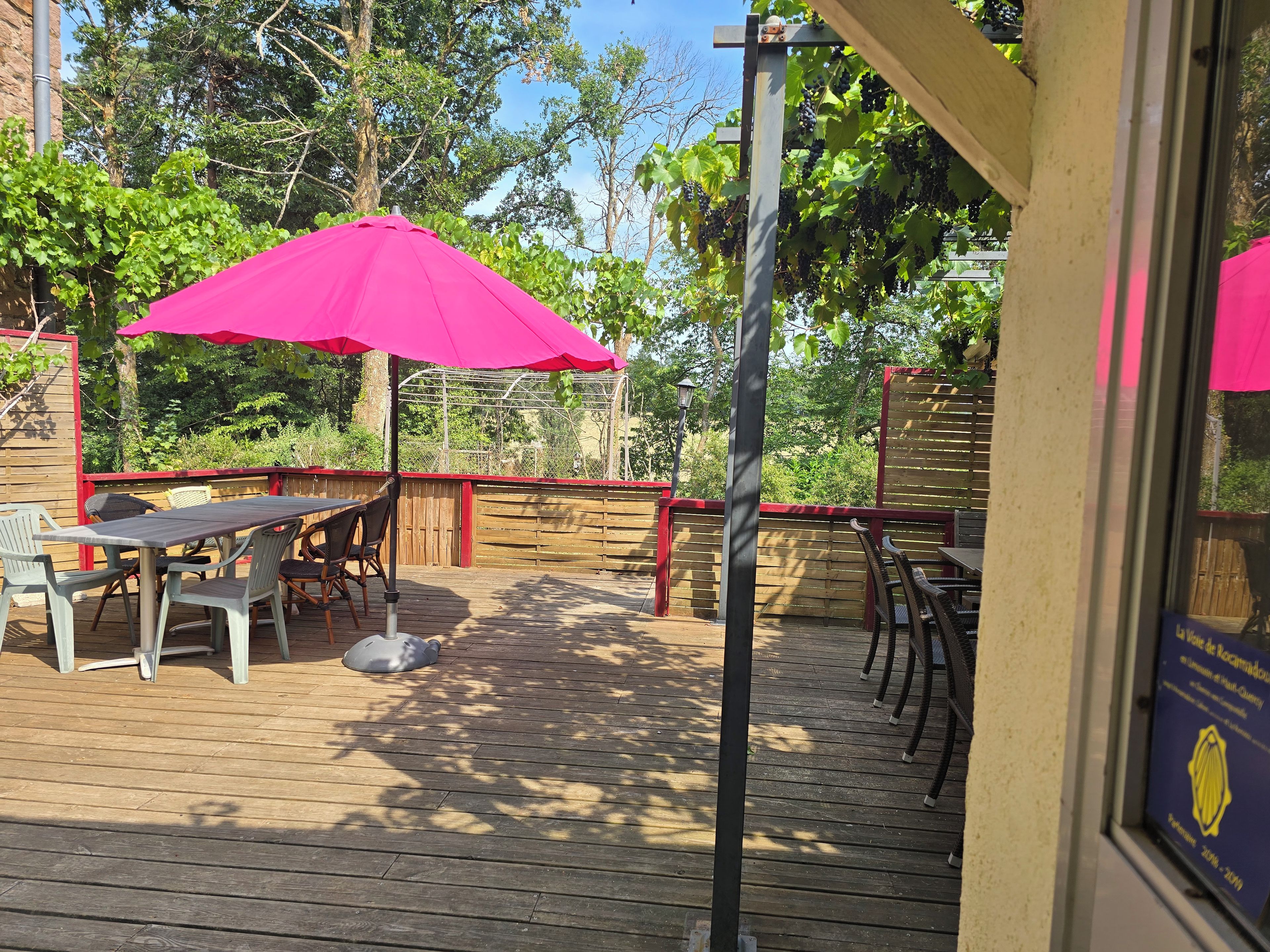 Une terrasse extérieure avec des tables et des chaises en bois, un parasol rose et une clôture en bois.