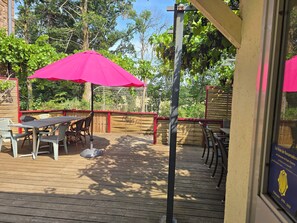 Une terrasse extérieure avec des tables et des chaises en bois, un parasol rose et une clôture en bois.