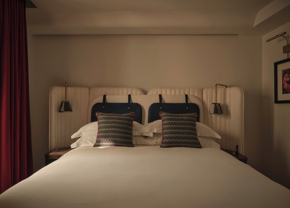 A hotel room with a large bed, two pillows, a headboard, bedside lamps, and a red curtain.
