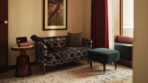 A room with a patterned sofa, a small round table, a framed picture on the wall, and a window with curtains. - The Shepherd Mayfair (London)