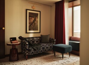 A room with a patterned sofa, a small round table, a framed picture on the wall, and a window with curtains.