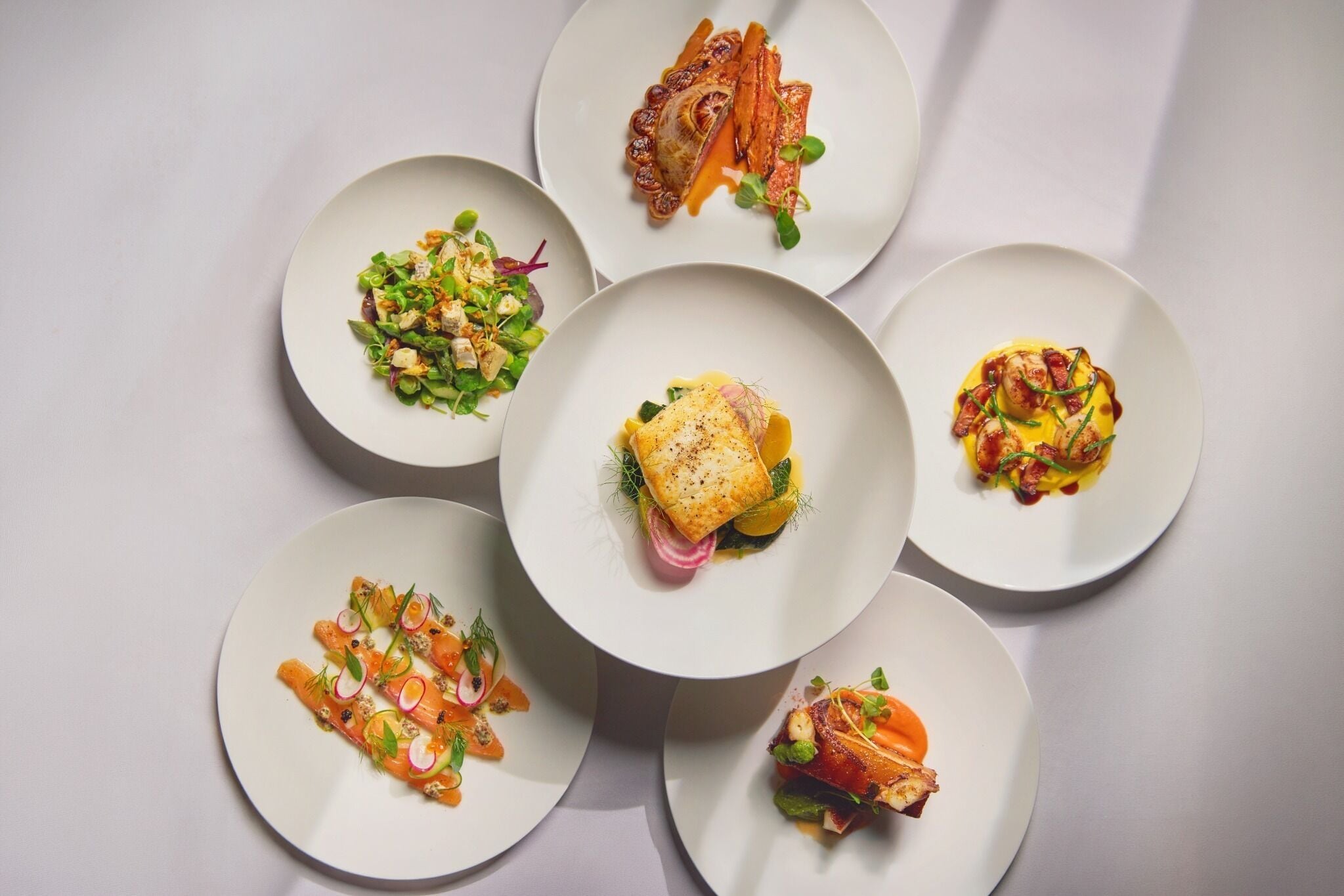 A top-down view of a dining table with six plates of food.