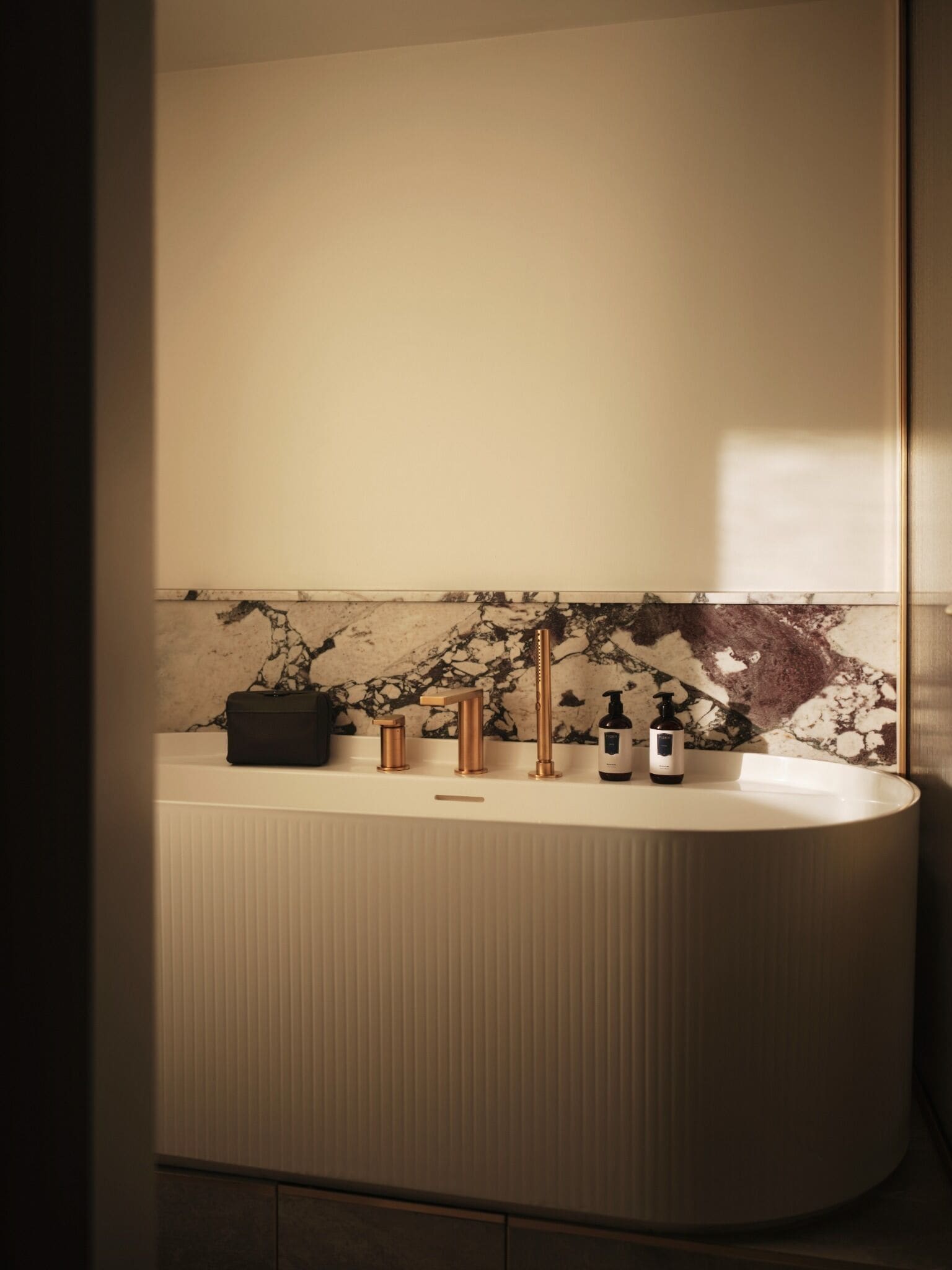 Een moderne badkamer met een marmeren spatwand, een vrijstaand bad en twee handpompen.