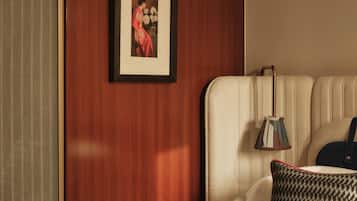 Ein Hotelzimmer mit einer Holzwand, einem gerahmten Bild, einer Nachttischlampe, einem gemusterten Kissen und einem roten Gegenstand auf dem Bett.