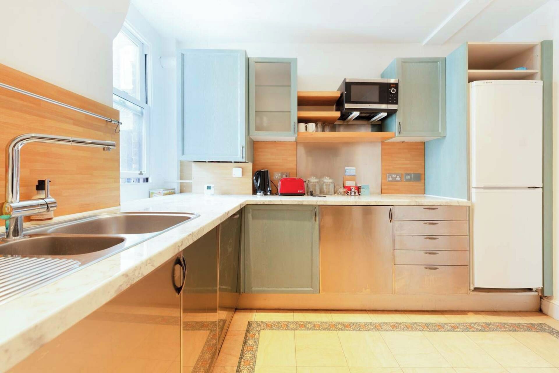 Une cuisine moderne dotée d’un évier à deux bacs, d’appareils électroménagers en acier inoxydable et de meubles de couleur bleu clair.