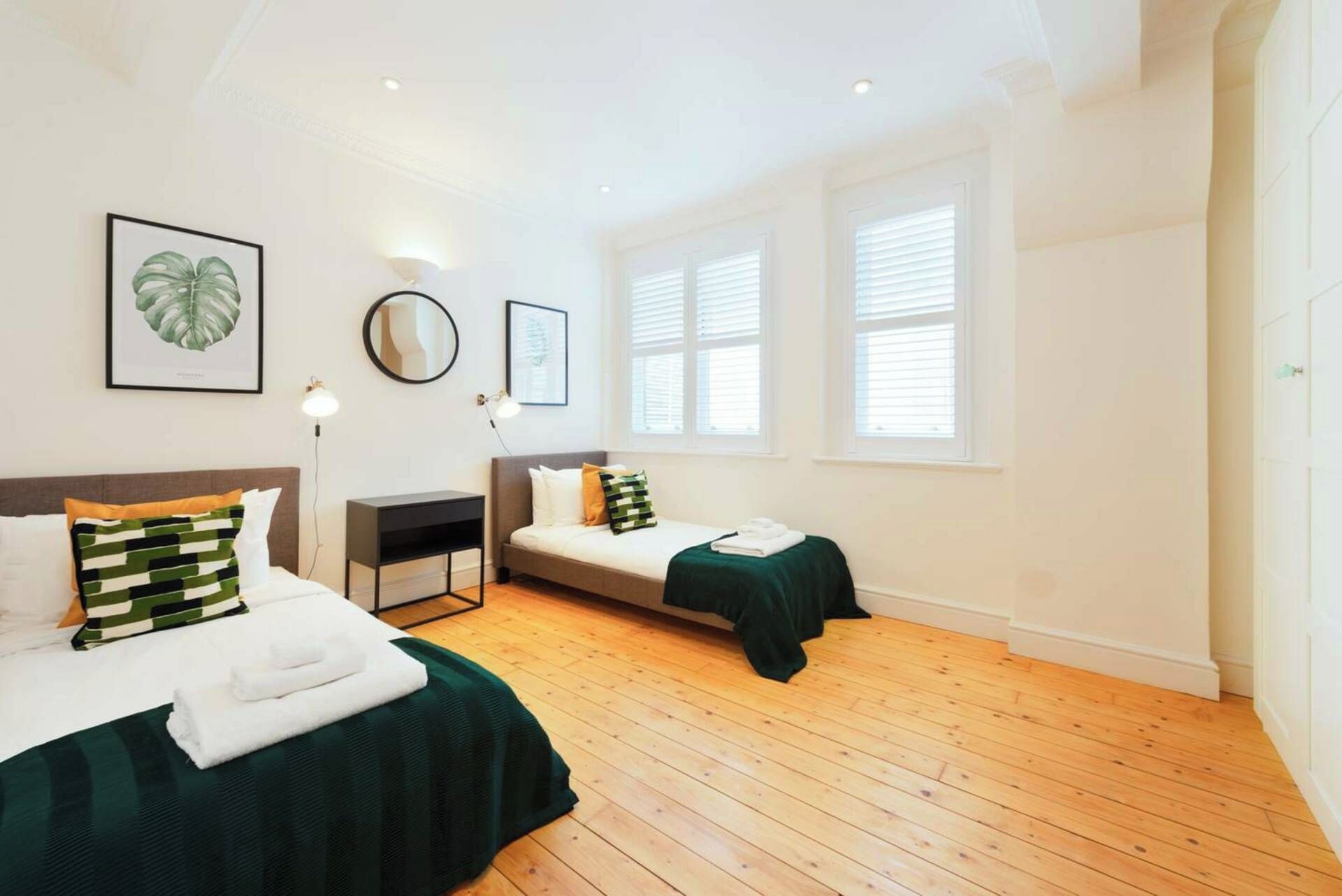 Une chambre avec deux lits, une table de chevet, un miroir et des œuvres d’art encadrées accrochées au mur.