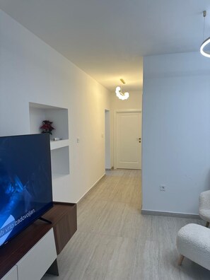 Un salon moderne avec un téléviseur à écran plat, un canapé blanc et un couloir menant à une porte.