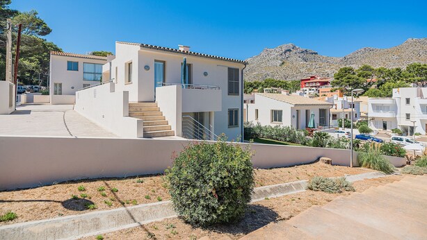 A modern two-story building with a flat roof, a staircase leading to the upper floor, and a small garden area with a bush. - Seaside Escape in Cala Sant Vicenc (Pollença)