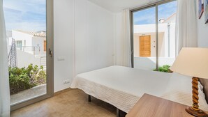 A bedroom with a bed, a nightstand, a lamp, a sliding glass door, and a view of the outside. - Seaside Escape in Cala Sant Vicenc (Pollença)