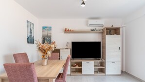 A modern living room with a wooden dining table, matching chairs, a flat-screen TV, and built-in storage cabinets.
