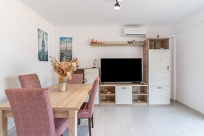A modern living room with a wooden dining table, matching chairs, a flat-screen TV, and built-in storage cabinets.