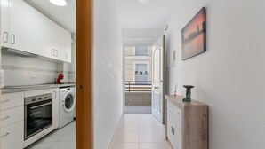 A modern kitchen with white cabinets, a washing machine, and a dining area with a view of the cityscape.