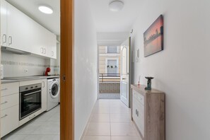 A modern kitchen with white cabinets, a washing machine, and a dining area with a view of the cityscape.