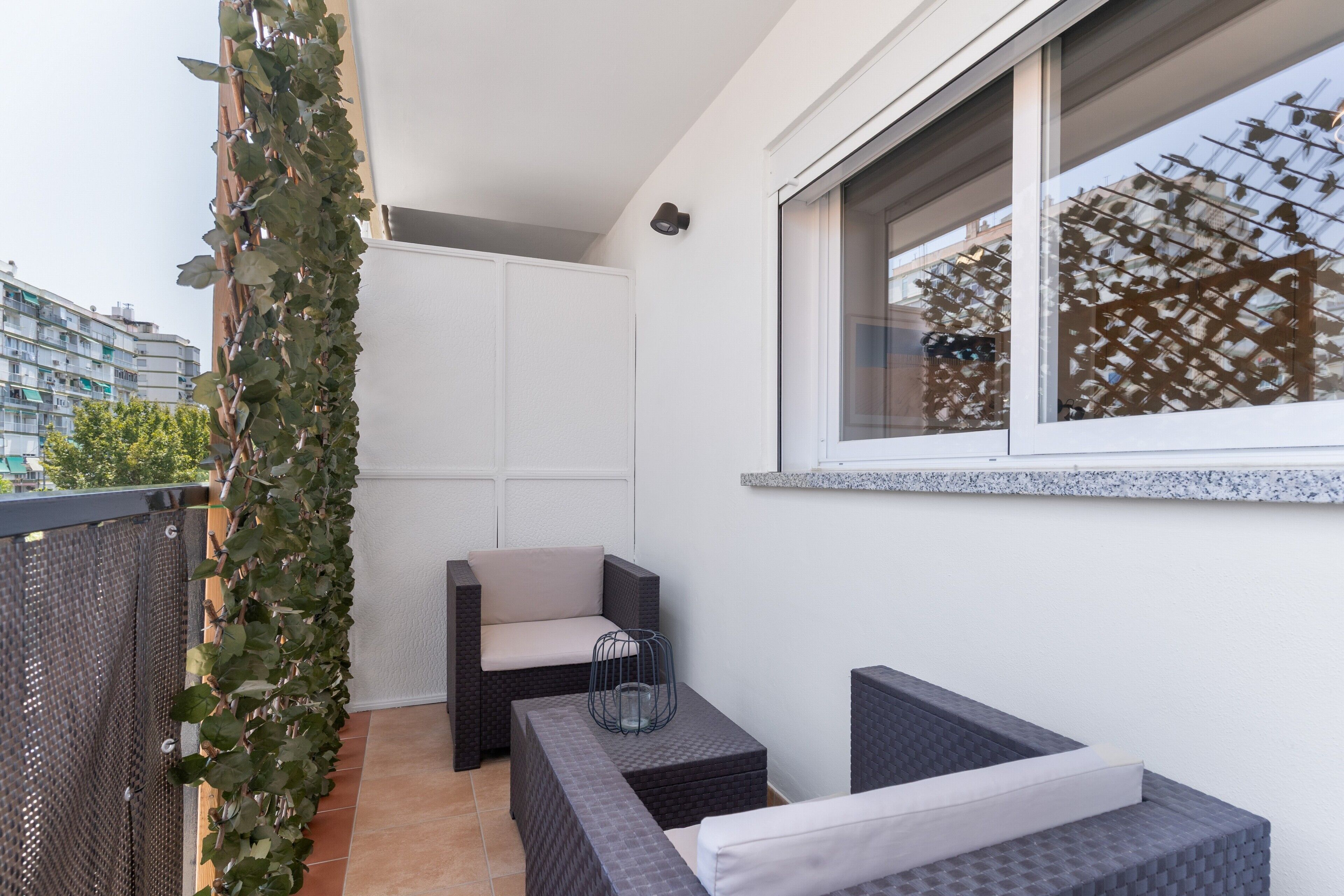 Een balkon met een rieten stoel, een tafeltje en een potplant.