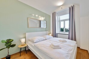 A hotel room with a bed, a bedside lamp, a potted plant, and a window with curtains. - Elegant Apartment Near City Center with Bike Path (Hlavní město Praha)