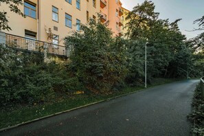 A narrow urban street with a sidewalk, dense foliage, and multi-story buildings with balconies. - Elegant Apartment Near City Center with Bike Path (Hlavní město Praha)