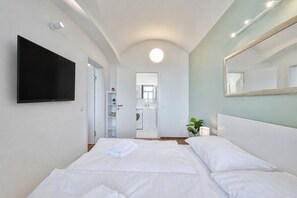 A hotel room with a bed, a television, a mirror, and a view into the bathroom. - Elegant Apartment Near City Center with Bike Path (Hlavní město Praha)