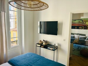 Een slaapkamer met een bed, een aan de muur bevestigde televisie, een nachtkastje met decoratieve objecten en een raam met gordijnen.