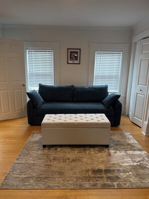 A living room with a dark blue sofa, a white ottoman, and a patterned rug.