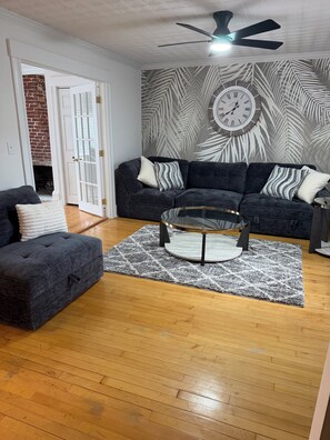 A living room with a dark grey sofa, a glass coffee table, and a patterned rug.