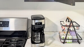 Une cuisine équipée d’un four à micro-ondes, d’une machine à café et d’une étagère où sont rangés des verres et des tasses.