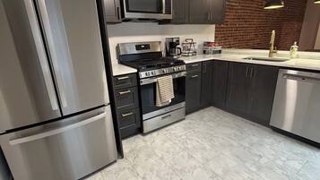 Une cuisine moderne dotée d’appareils électroménagers en acier inoxydable, d’un mur décoratif en briques et d’un ventilateur de plafond.