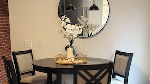 Un coin repas comprenant une table ronde, quatre chaises, un vase de fleurs et un miroir fixé au mur.